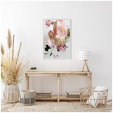 Light wooden console table beneath a framed canvas featuring soft pink and cream flowers against a white wall, surrounded by neutral-toned wicker accents and dried grasses.
