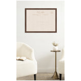Framed linen fabric pinboard designed like a vintage postcard hangs on a white wall above a brass side table between two cream-colored upholstered chairs.