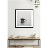 Black and white framed photo of a humpback whale breaching the water, hung above a wooden shelf holding books, a mug, a white vase, and decorative beads.