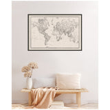 Black and white vintage-style world map framed in black and white linen, hanging above a minimalist wooden bench with white pillows and beige throw blanket.