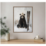Painting of a black bear sitting in snow wearing a beige knit hat, with vintage wooden skis standing upright beside it, all framed and hung on a pale wall.