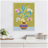 Framed canvas of stylized snowdrop flowers with blue-green stems and multicolored petals in a patterned vase on olive and pale blue background above a white dresser.