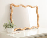 Rectangular mirror with a wavy scallop edge frame made of light tan rattan, resting on a white surface near a small green potted plant.