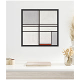 Framed abstract painting with black grid lines dividing white, gray, and a small red rectangle, hung on a white wall above a light wood table with pampas grass and small containers.