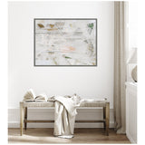Abstract framed canvas wall art with white, beige, and touches of green and peach, hanging above a wooden bench with an open book and a draped cream-colored cloth.