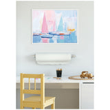 Abstract sailboat harbor painting with pastel pink and blue sails above a white desk holding art supplies and a wooden toy car, framed against a pale wall.