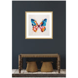 Framed colorful butterfly artwork with bold blue and orange brush strokes, hanging on a dark gray wall above a rustic wooden bench with two woven baskets underneath.