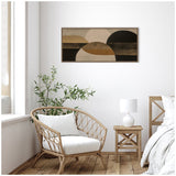 Framed abstract canvas art with layered neutral-toned semicircles in black, brown, beige, and tan on a white wall above a wicker chair, wooden nightstand, and white lamp.