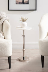 Small adjustable side table with round white marble top and chrome metal base, between two cream upholstered chairs with black legs on light wood floor.