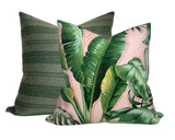Two square pillows, one with large green palm leaves on a soft pink background and the other with textured dark and light green horizontal stripes.