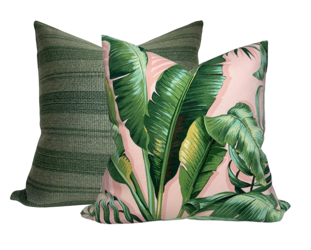 Two square pillows, one with large green palm leaves on a soft pink background and the other with textured dark and light green horizontal stripes.