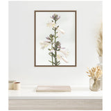 Framed canvas print of a tall green hosta stem with white and pale lavender flowers against a soft gray background, displayed above a light wood surface with dried floral decor.