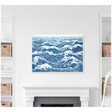Framed canvas showing abstract blue and white linocut waves with swirling patterns, hanging above a white fireplace in a room with white shelves and wicker baskets.