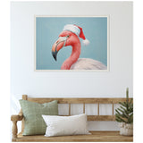 Close-up portrait of a pink flamingo wearing a red and white Santa hat, set against a soft blue background, in a white beaded frame hung above a wooden bench with cushions and a small potted pine.