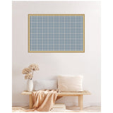 Rectangular light blue plaid fabric pinboard with a thin wood frame hanging above a minimalist wooden bench with pale cushions and a light beige throw.