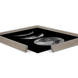 Square framed print depicting four monochrome moon phases from crescent to full against a solid black background in a light wood frame shown at an angle with two corners cut away