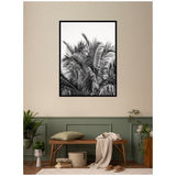 Black and white framed photograph of palm tree fronds against a plain wall, above a wooden bench with a green cushion and beige throw in a decorated room.