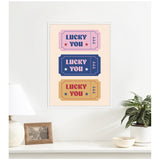 Framed canvas print with three stylized vintage tickets in pink, blue, and tan, each featuring 'LUCKY YOU' and '777' with star accents.