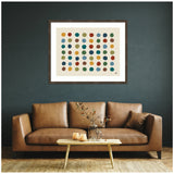 Abstract wall art print titled Meditation No. 3b by Kelly Knaga, featuring rows of colorful dots in mustard yellow, red, green, and blue, framed in dark wood above a brown leather sofa.
