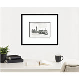 Black and white framed ink drawing of London’s Houses of Parliament and Westminster Bridge hanging above a white desk with books, an open notebook, a black mug, and a potted plant.