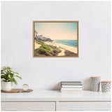 Framed vintage coastal beach scene with sandy shore, green shrubbery, and ocean waves under a clear sky, hanging on a white wall above a white shelf.