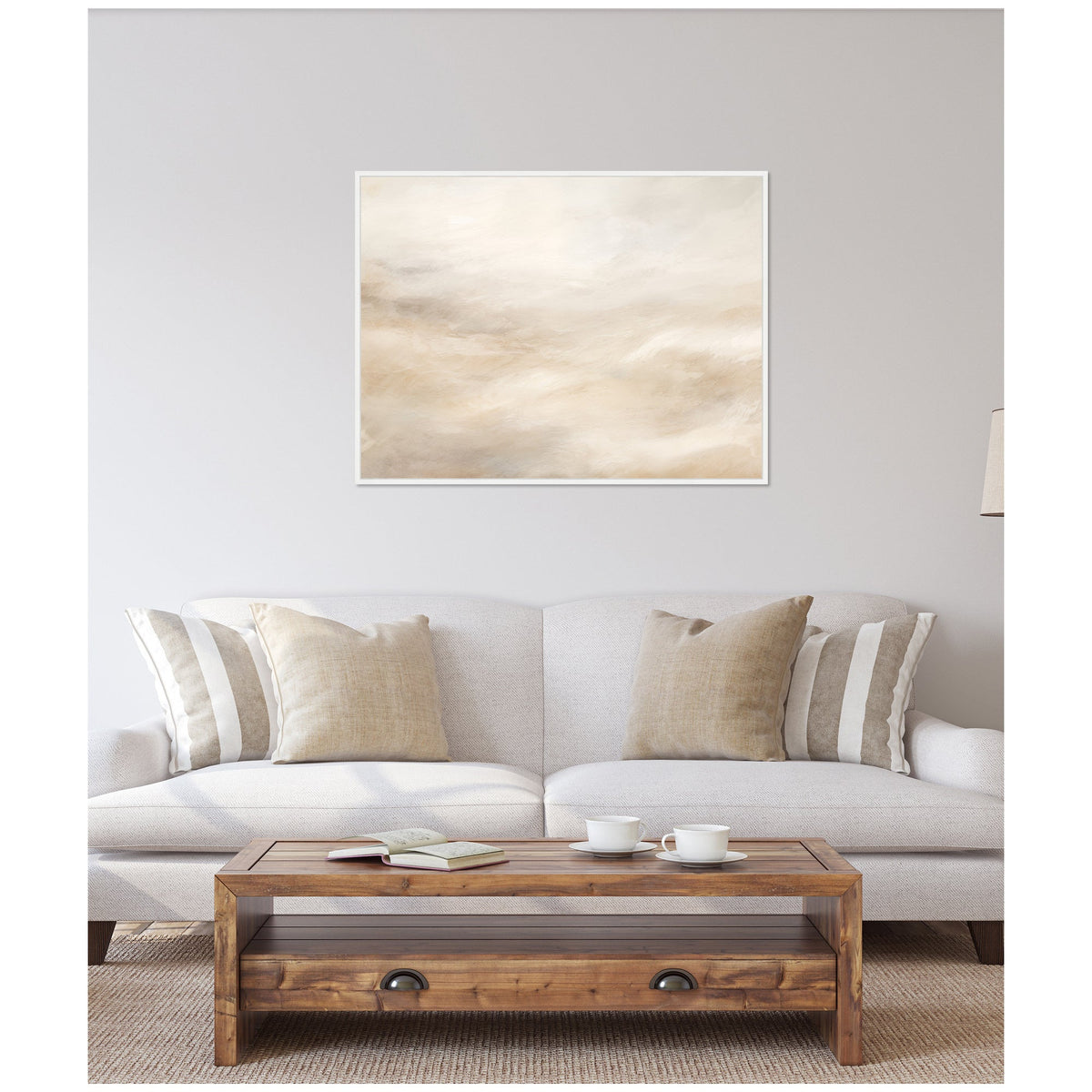 Abstract white and beige textured canvas with tonal soft gradients above a beige sofa with striped and solid cushions, and a wooden coffee table with cups and books.