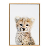 Portrait of a young cheetah cub with golden fur and black spots on a white background, framed in light wood.