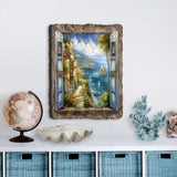 Wall art depicting a seaside village viewed through open blue shutters framed by rustic wood, with cliffs, sailboats, and lush greenery under a partly cloudy sky.