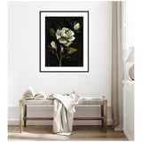Framed art print of a white rose with green leaves on a dark background, hanging above a wooden bench with an open book and cream-colored fabric draped over it.
