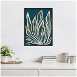 Framed canvas artwork depicting abstract elongated leaves with green and cream tones on a deep blue background, hanging above a white cabinet with decorative items.