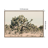 Framed canvas wall art depicting a desert scene with a large, green Joshua tree in the foreground and several smaller Joshua trees in the background under a pale sky.