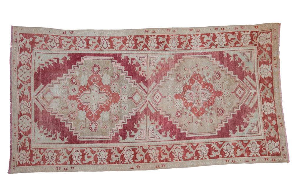 Rectangular vintage distressed Oushak carpet with faded red and cream geometric and floral patterns, featuring two large central medallions and a decorative border.