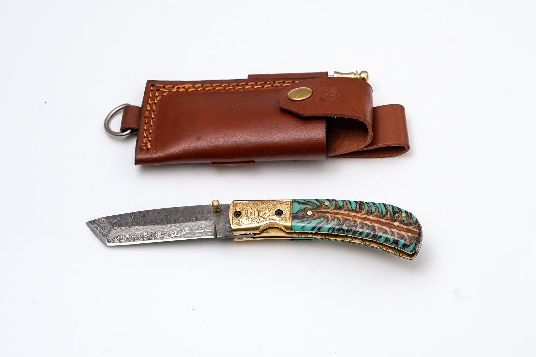 Hand-Forged Damascus Tanto Folder with teal pine cone handle, engraved brass bolster, and fire starter in leather sheath