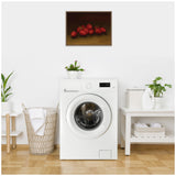 Still life painting of red strawberries clustered on a dark brown surface with subtle shadows, framed in wood and hung on a white wall above a washing machine.