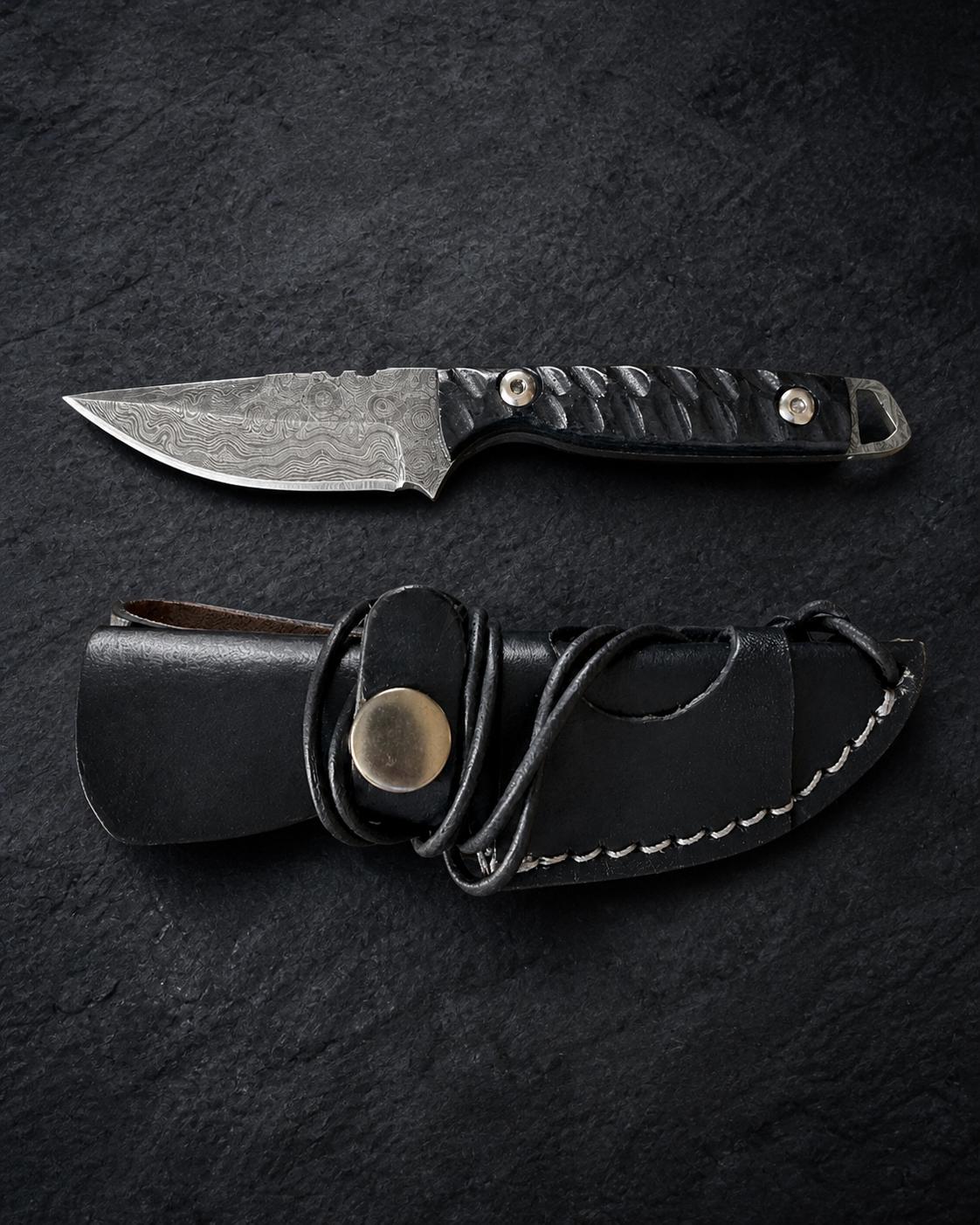 Titan "Shadow Scale" Damascus Hunting Knife with drop-point blade and carved black micarta handle resting on a dark surface