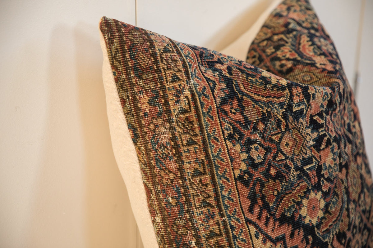 Close-up of a 24x24 pillow featuring an intricate vintage rug fragment pattern with earthy tones, dark blue accents, and worn texture on a light background.