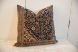 Square pillow featuring a dark navy background with intricate floral and geometric patterns in muted reds, tans, and greens, bordered by a patterned band.