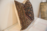 Square pillow with a vintage rug fragment design featuring intricate geometric patterns in navy, rust, and cream colors on natural light fabric sides.
