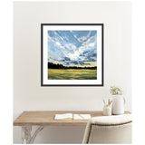 Square framed painting showing a cloudy sky with dynamic blue and white brushstrokes over a dark tree line and yellow-green grass field, hanging above a wood desk with open notebook and white vase.