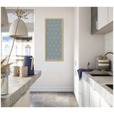 Tall narrow blue botanical block print with white floral motifs framed in light wood, hanging on a white wall in a modern kitchen with concrete countertops and ceramic mugs.