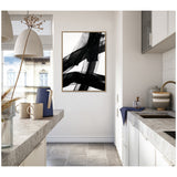 Minimalist kitchen with concrete countertops and white cabinets features framed abstract black brushstroke art on the wall, accented by dried stems in glass on the counter.