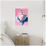 Framed canvas painting of a conch shell in pastel colors on bright pink background, displayed on a neutral wall above a rustic wooden side table with books and a cup.
