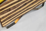 Close-up of a striped wooden surface with alternating mocha and natural wood tones, featuring a metal handle with a hammered texture underneath.