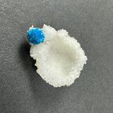 Bright blue cavansite crystal ball attached to white, crystalline stilbite with a sparkling texture on a dark background