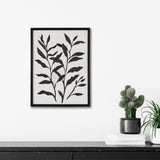 Black silhouette of botanical leaves with elongated shapes on a white background framed in black, hanging above a dark wood surface with potted cacti and books.