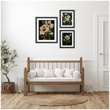 Three framed floral prints with white and yellow flowers on black backgrounds, arranged above a wooden bench with white cushions in a minimalist room with wood floor and a potted plant.
