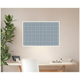 Light blue plaid fabric pinboard with white grid lines in a white frame, mounted on a beige wall above a wooden desk with books and a plant nearby.