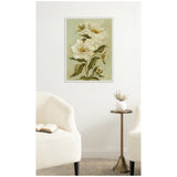 Framed canvas print of white flowers with green leaves on a muted green background, hung on a white wall between two off-white armchairs with a round brass side table.