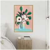 Framed painting of white flowers with green leaves in a blue vase against a soft pink background, hanging above a rustic wooden bedside table with books and a cup.