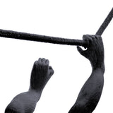 Close-up of a black sculpted monkey arm and hand gripping a textured black rope against a white background.